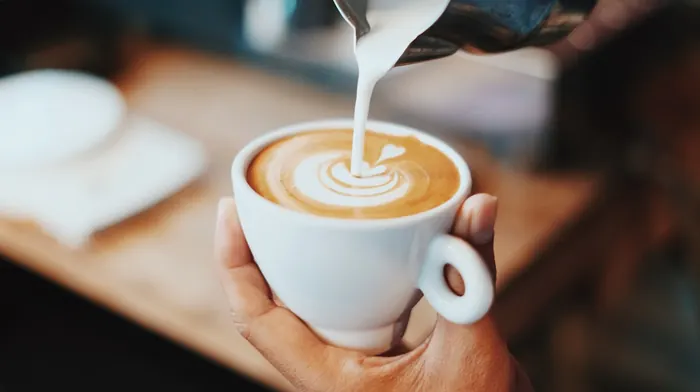 Filiżanka latte z mlecznym wzorem trzymana w dłoni